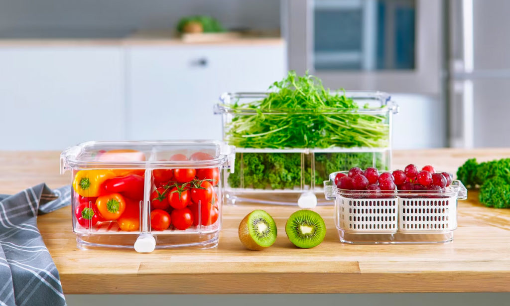 Grønnsaker og frukt i gjennomsiktige oppbevaringsbokser på kjøkkenbenk