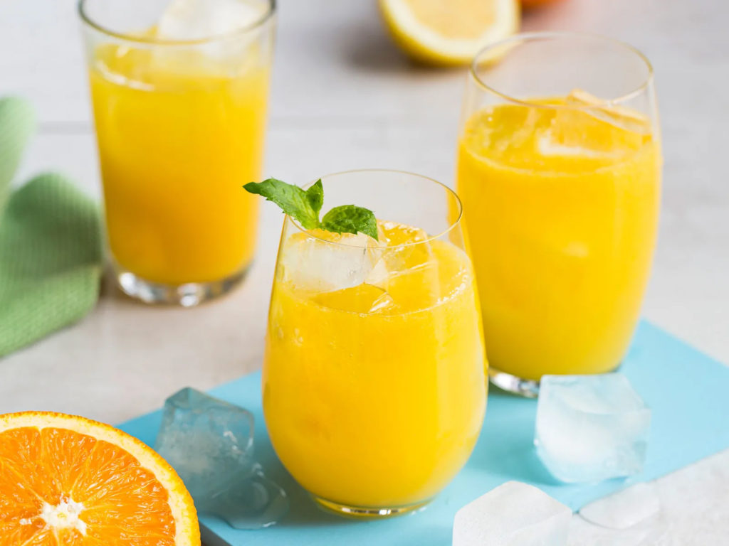 Glass med appelsinjuice og isbiter stående på et lyseblått brett