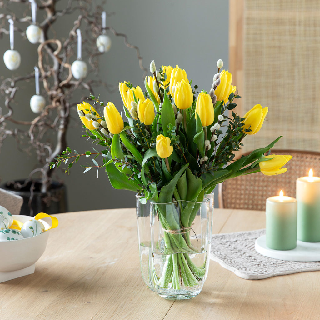 Bukett av gule tulipaner i en gjennomsiktig vase på et trebord