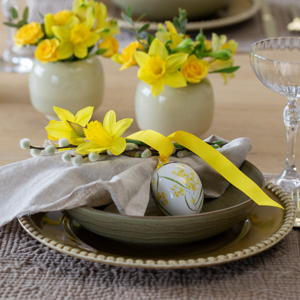 Borddekking med tallerken og skål til påske med påskeegg, serviett med gult bånd og gåsunger